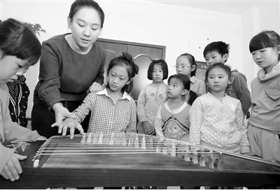 10月11日,在河北省邢台市桥东区三义庙社区“儿童之家”,小女孩张佳欣在邢台华艺音乐培训机构教师杨赛男的指导下感知古筝。